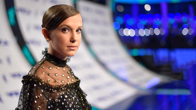 HD-wallpaper-millie-bobby-brown-is-wearing-black-and-gold-color-dress-standing-in-blur-background-girls